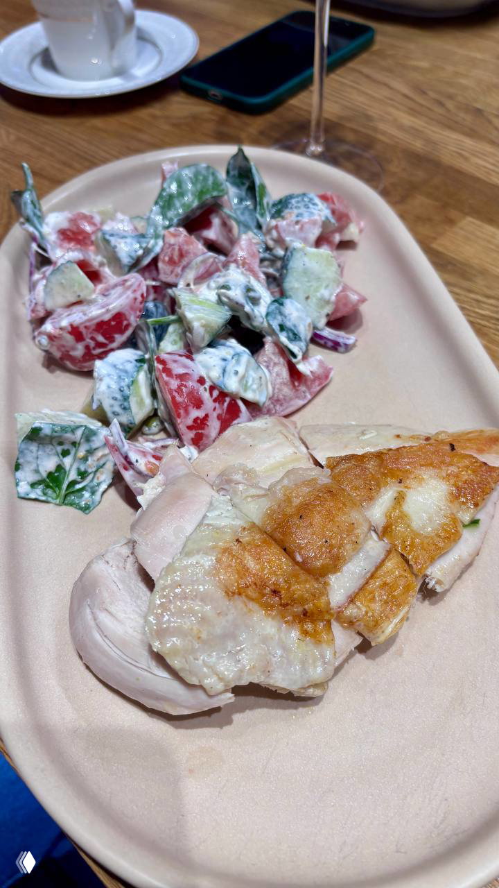 Овальная тарелка с кусочком жареной курицы и кремовым салатом из помидоров и огурцов — простая домашняя подача в заведении.