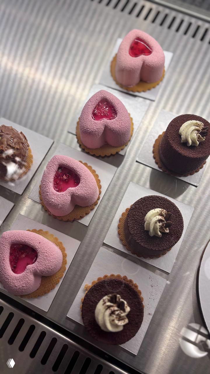 Витрина десертов: маленькие розовые сердечки и шоколадные пирожные в охлаждающем лотке — аккуратная и привлекающая подача.