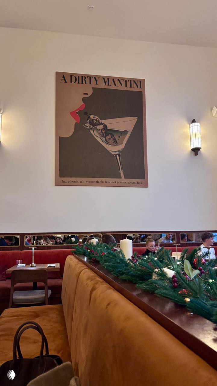 Стена с постером «A Dirty Mantini», рождественские гирлянды и часть зала с диванами и столиками в тёплых тонах.