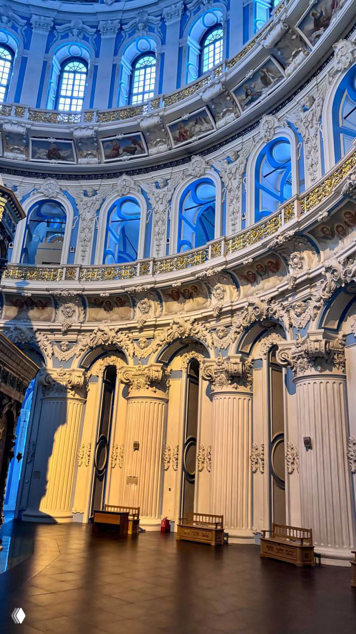 Колонны и аркады внутри собора: высокий барабан с окнами, рельефная лепнина и теплое освещение, создающее контрасты с синими стенами.