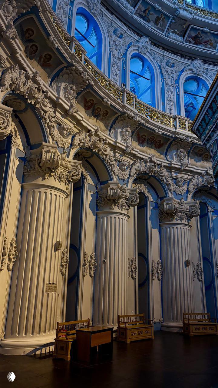 Фрагмент интерьера с декоративными колоннами и балконами: барочная отделка, золочёные элементы и повторяющаяся орнаментальная структура.