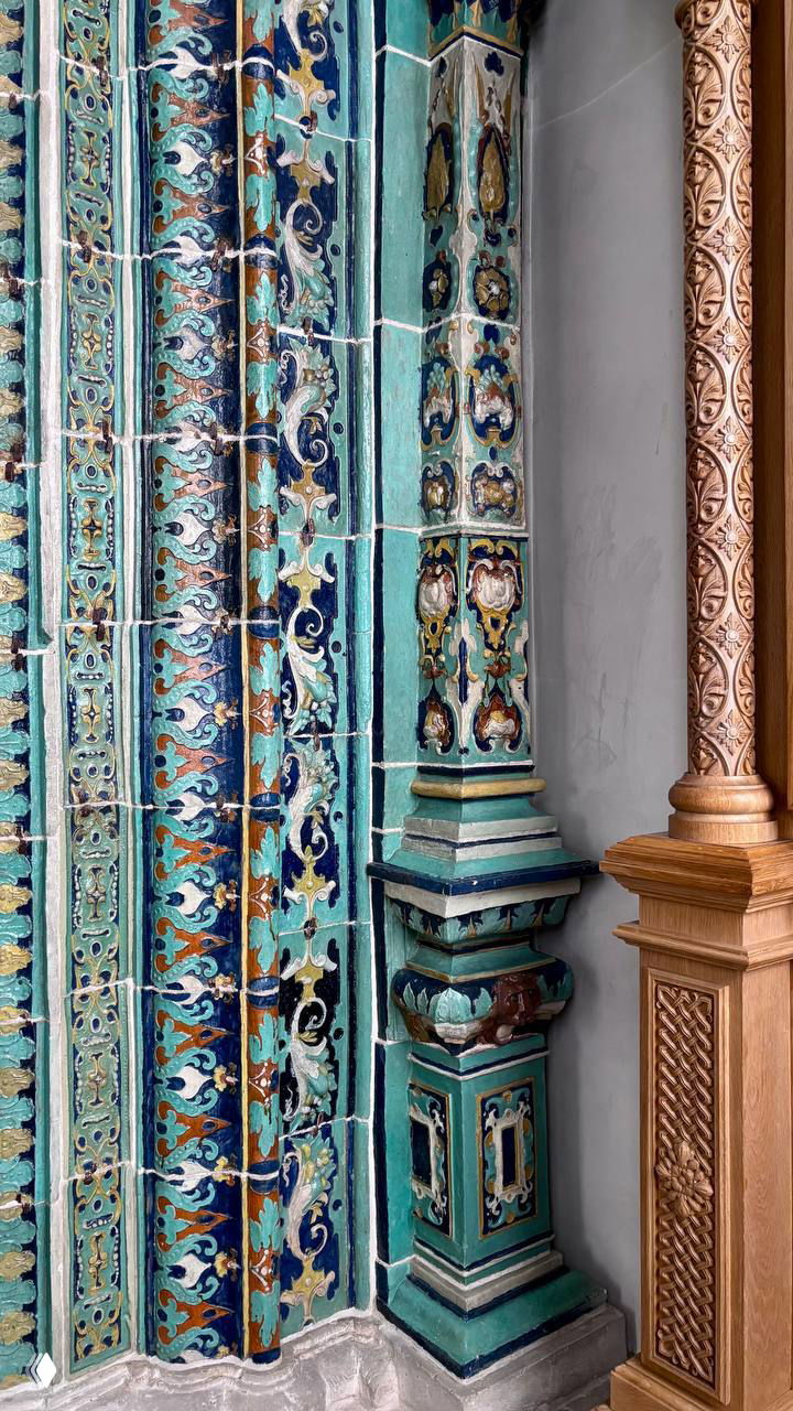 Крупный план изразцовой облицовки и резных деревянных деталей у входа: бирюзовые плитки с растительным орнаментом и тонкая резьба по дереву.