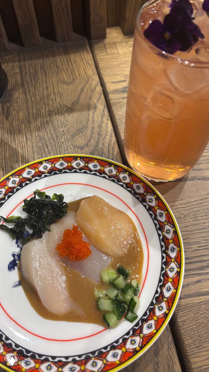 Тарелка с сашими или закуской: гребешок, икра, маринованные огурцы и водоросли рядом с ярким прохладительным напитком.