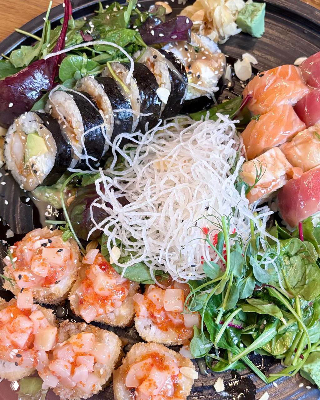 Тарелка с ассорти роллов и миксом салатов: рядом хрустящие жареные роллы, зелень, имбирь и васаби — подача в ресторане Sabzero