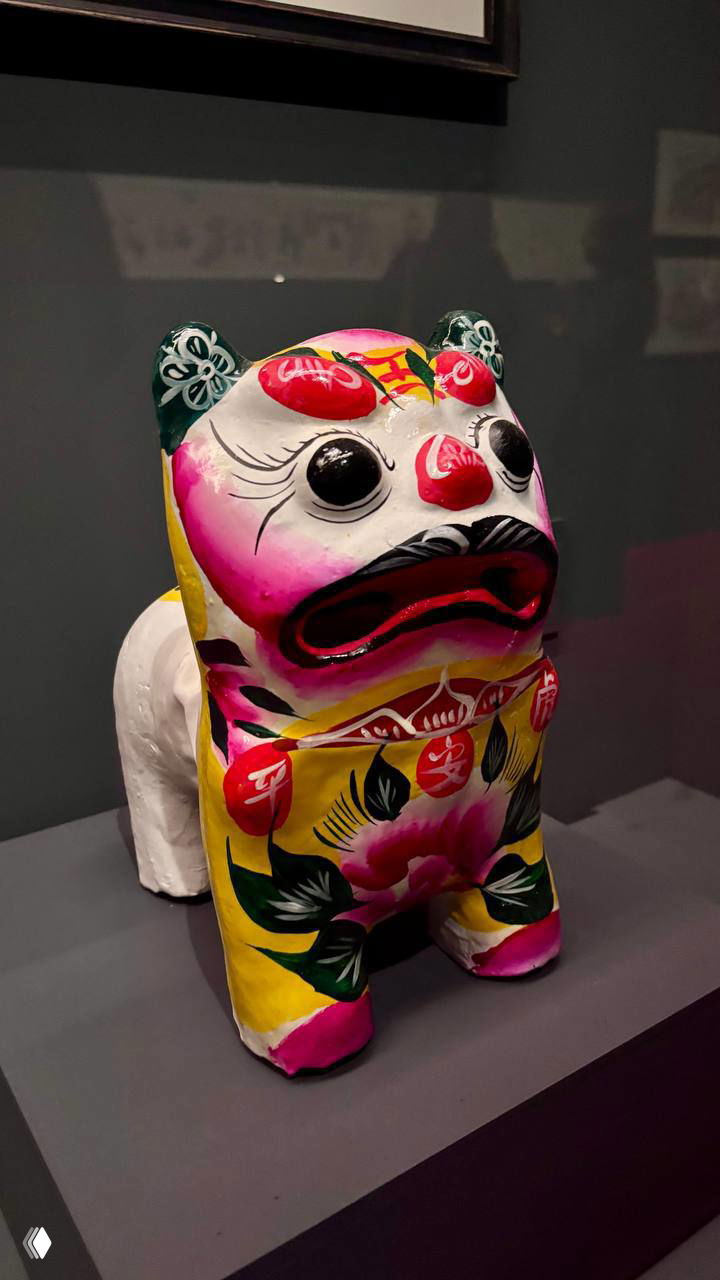 Ярко расписанная керамическая фигурка животного в традиционном китайском стиле с цветочными мотивами, выставленная на подиуме в музее как предмет народного искусства.