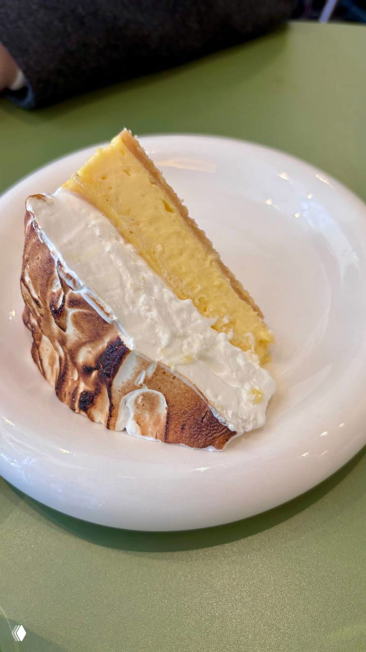 Кусок лимонного тарта с подожжённой меренгой и кремом на белой тарелке — десерт из меню Stim, крупный портрет лимонного тарта.