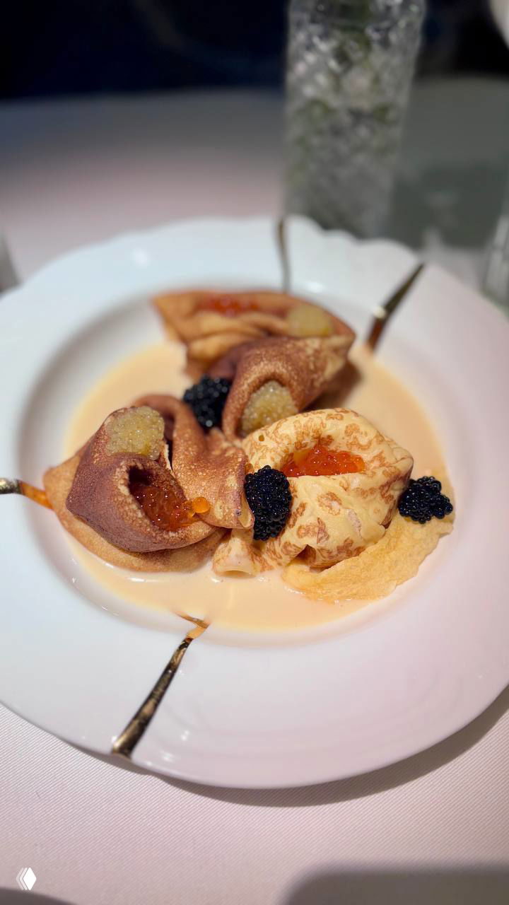 Порция тонких блинчиков с красной и чёрной икрой и кремовым соусом на белой тарелке, детализированная текстура и контрастная подача.