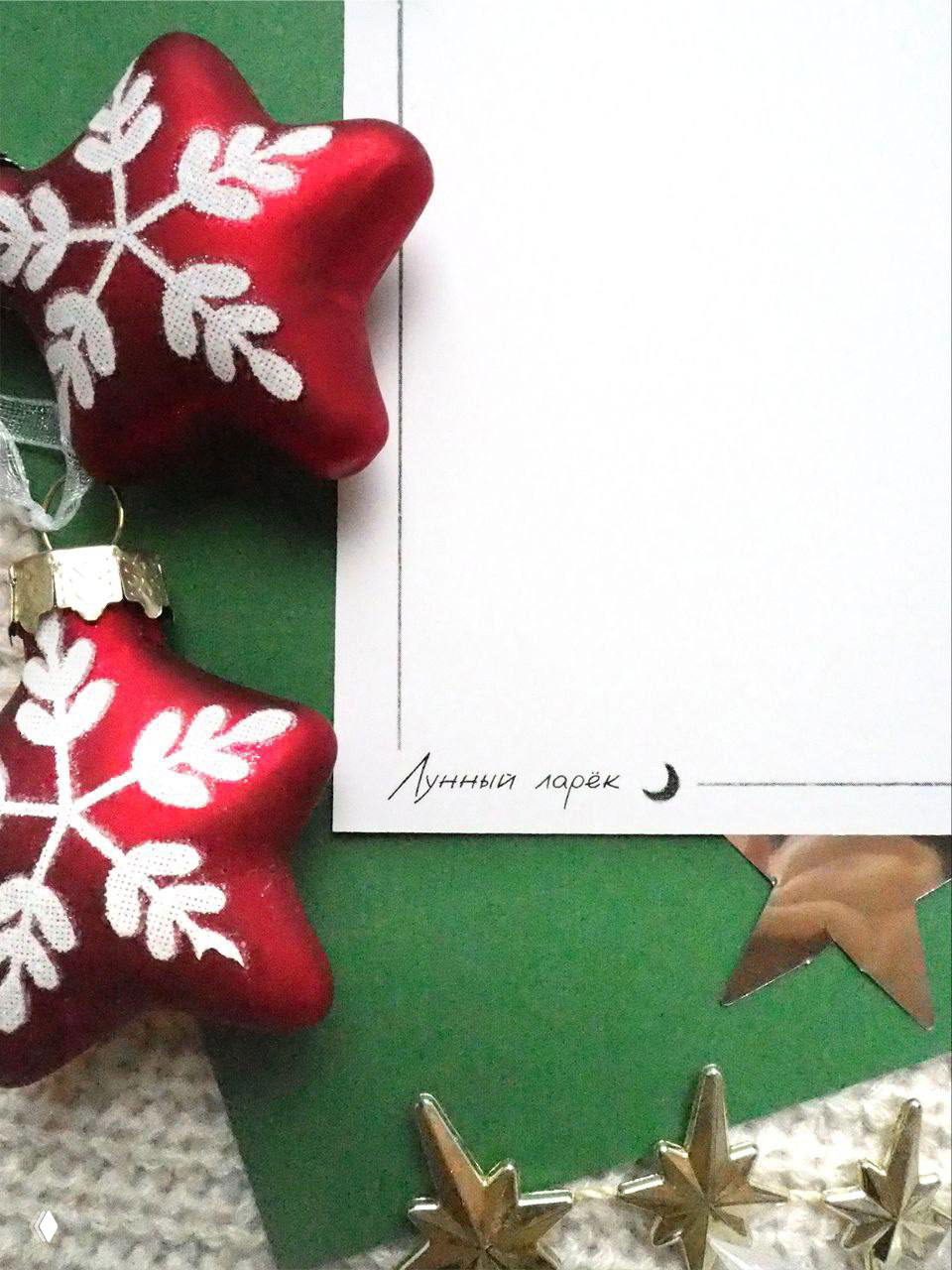 Фрагмент открытки на фоне рождественских игрушек: крафтовая карточка с логотипом «Лунный ларёк» и декоративными звёздами — атмосфера рукодельного подарка.
