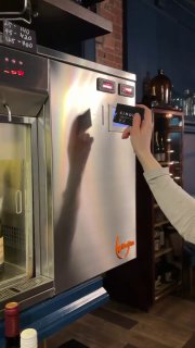 Рука сотрудника нажимает на панель эноматика в металлическом корпусе — процесс выбора и отбора порции вина картой или кнопкой в ресторане.