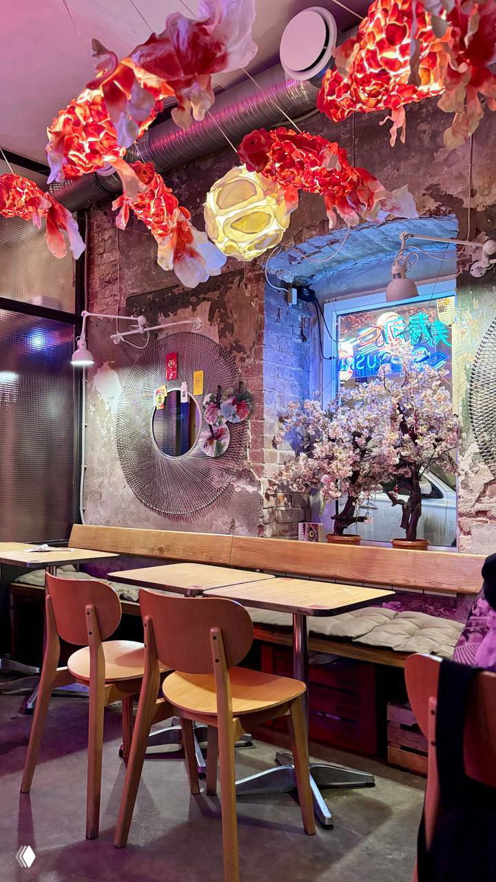 Интерьер с красно-золотыми подвесными декоративными рыбками и столиками; индустриальные стены и декоративная вишня создают стильное пространство для еды.