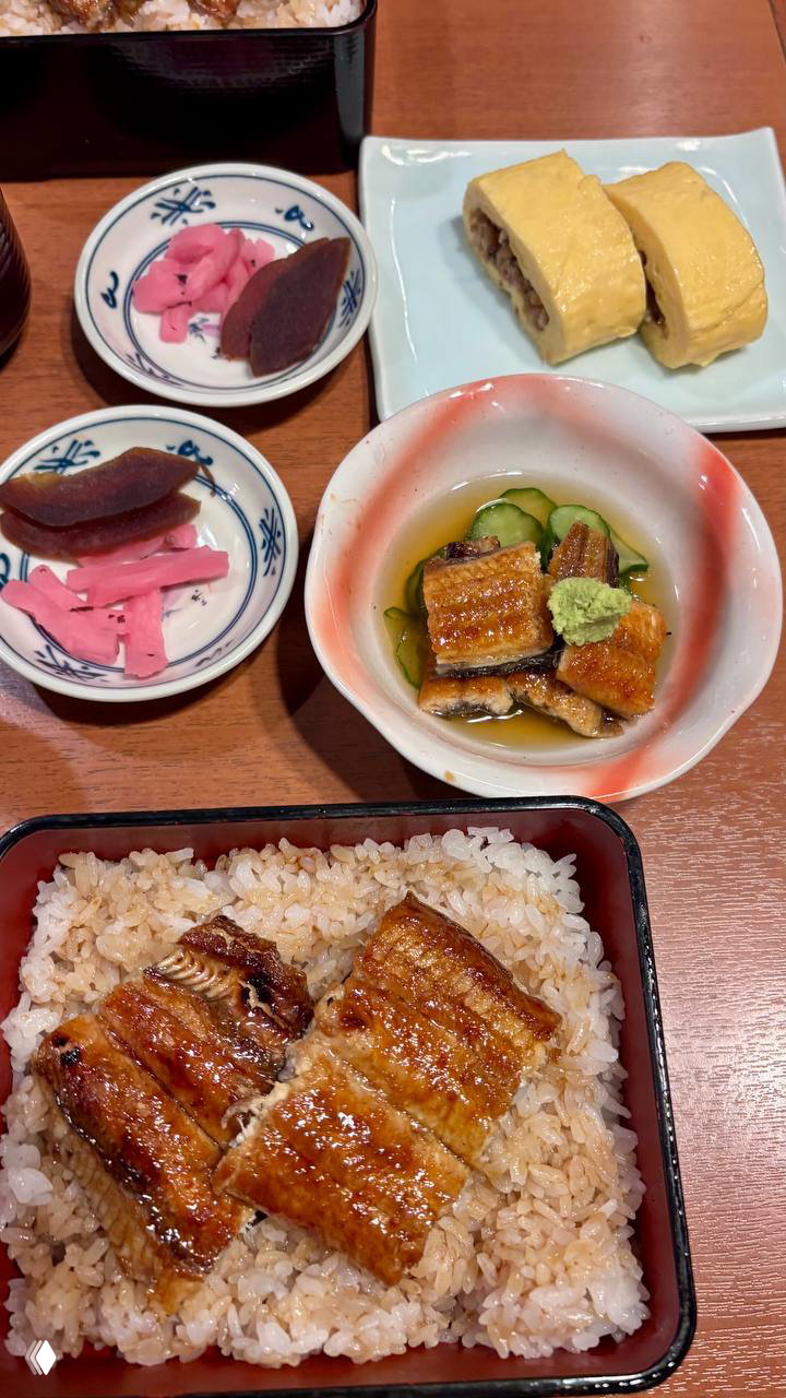 Традиционный обед унаги в коробке: запечённый угорь на рисе, миски с цукемоно и омлет тамаго на заднем плане — кадр из ресторана Uoi.