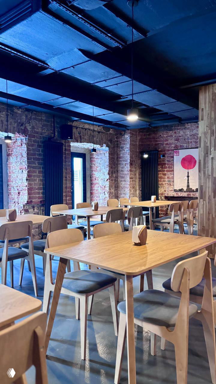 Зал ресторана с деревянными столами и стульями, кирпичными стенами и синим потолком — спокойная атмосфера японского кафе в центре Москвы.