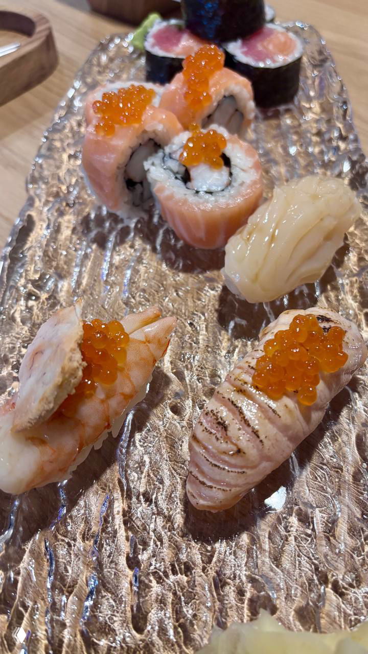 Еще один крупный план тарелки с ассорти суши, опаленные кусочки и урамаки с икрой, подача на прозрачной текстурной поверхности, вид с другой перспективы.