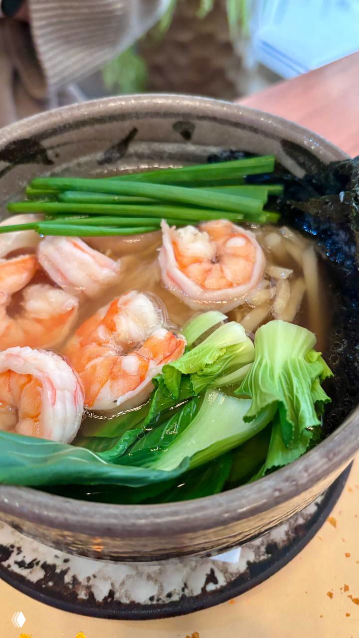 Чашка супа с лапшой, несколькими крупными креветками, листьями бок-чой и зелёным луком — горячее блюдо из посещённого места.