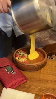 Официант в процессе наливания тягучего сыра прямо в тарелку с ингредиентами — демонстрация фондю в авторском стиле заведения.