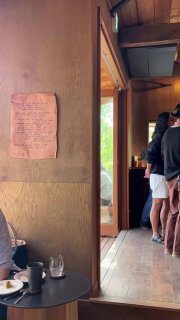 Узкий деревянный интерьер кофейни, на стене бумажный постер с текстом, люди стоят в очереди — уют и плотность пространства одновременно.