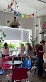 Интерьер кофейни Stim: разноцветные стулья, посетители у окна и свисающий диско-шар — атмосферный кадр зала в Басманном дворе.