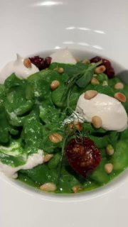 Крупный план зелёной пасты орикетти в Means: сочная паста со сливочно-шпинатным соусом, белыми кремовыми шариками, вялеными томатами и кедровыми орешками в тарелке.