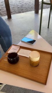 Минималистичный поднос с двумя чашками и небольшим десертом на светлом деревянном столе на открытой террасе — момент паузы за кофе.