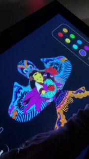 Экран с цифровым приложением для раскрашивания традиционной маски или воздушного змея; видна палитра цветов и рука пользователя во время интерактива.