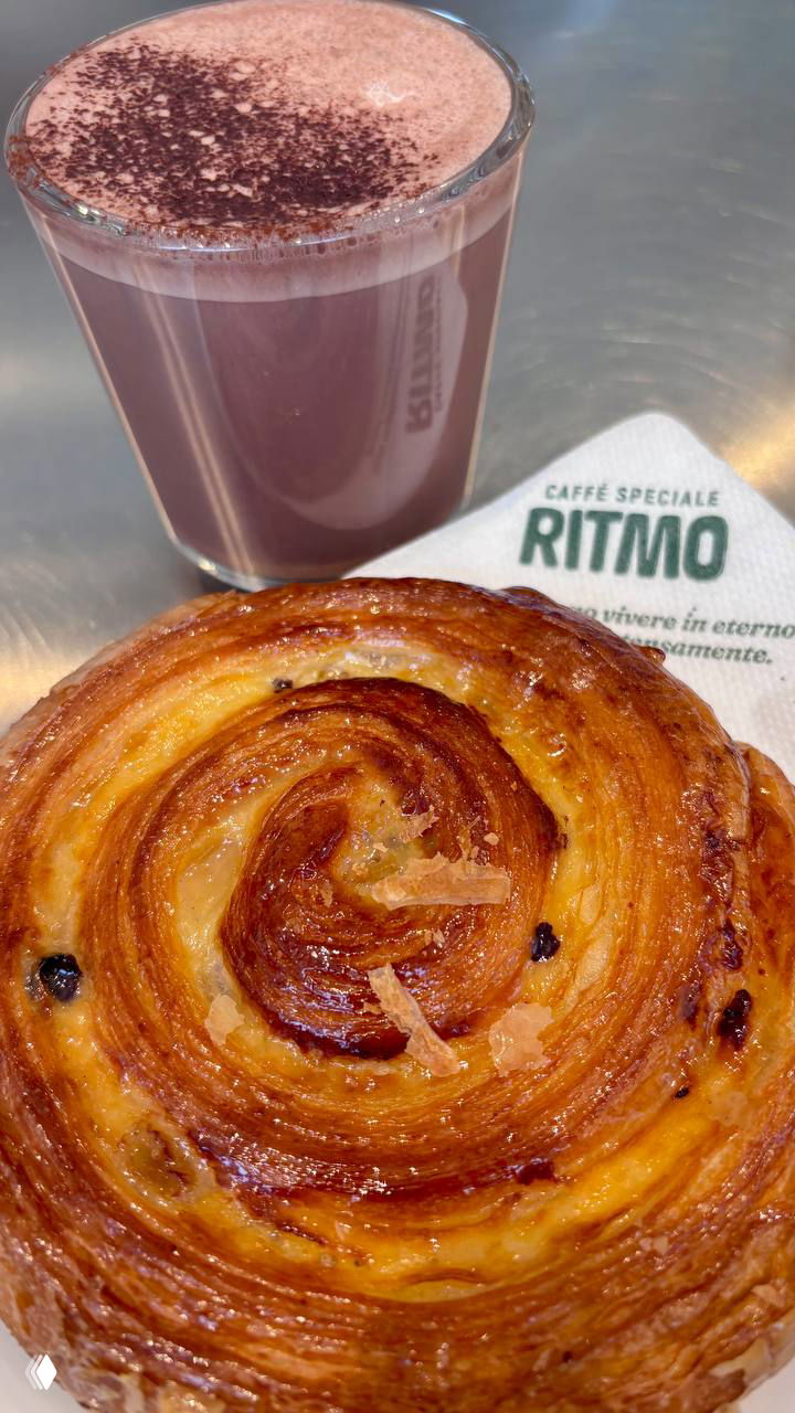 Крупный план: чашка тёплого чао-какао и апельсиновая булочка на салфетке с логотипом Ritmo — кадр из авторского обзора кофейни.