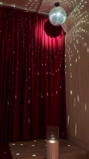 Отражения диско-шара и световые точки на красных занавесах, свеча на столе и часть сцены — атмосферный фрагмент интерьера бара Louis перед шоу.