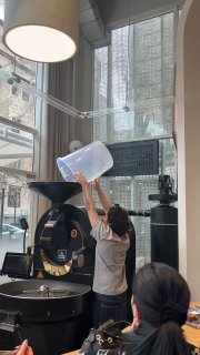 Рабочий процесс обжарки кофе: сотрудник высыпает зелёные зерна в большую обжарочную машину внутри кофейни, видно часть оборудования