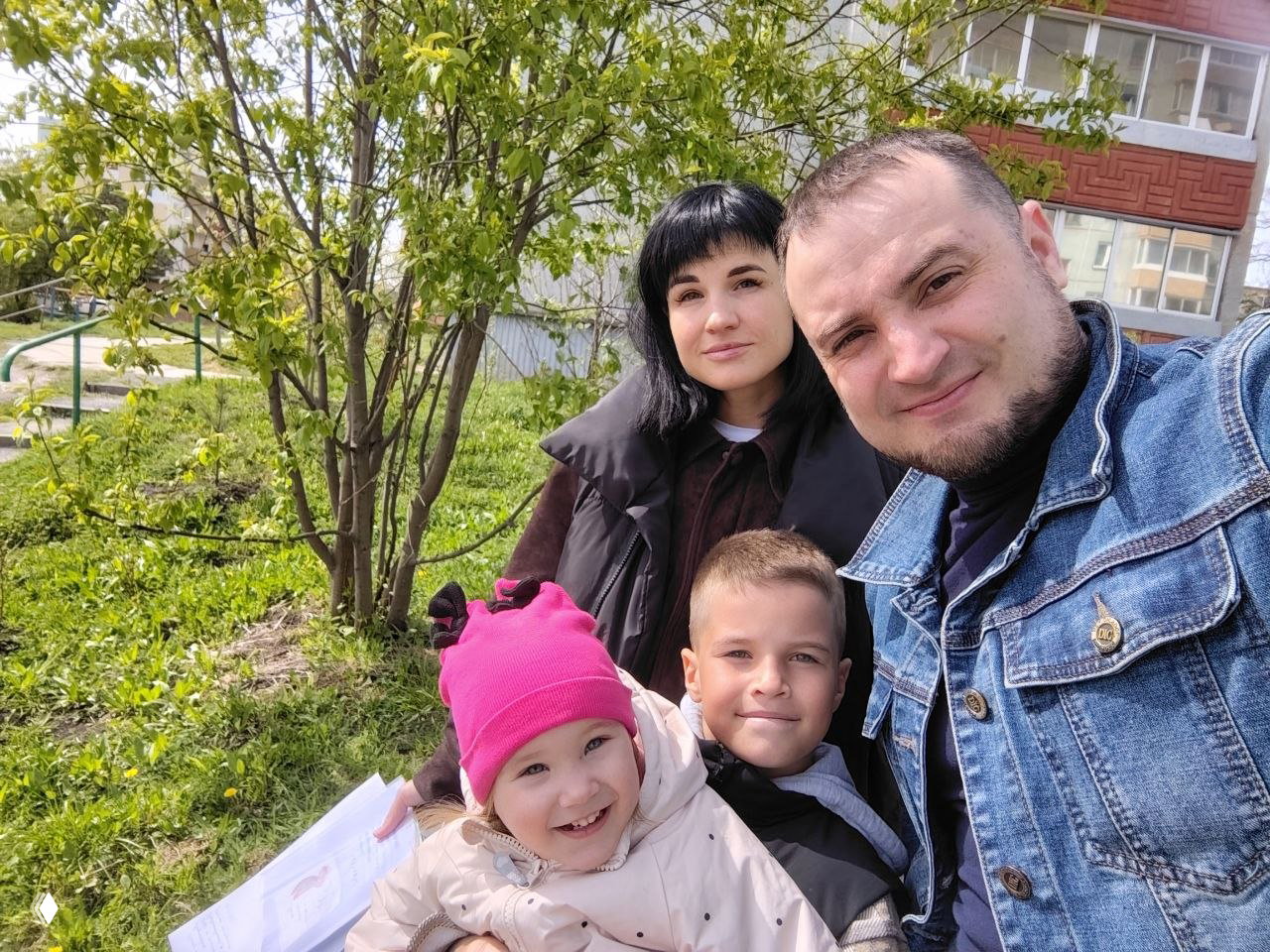 Селфи семьи на прогулке у жилого дома: родители и двое детей улыбаются; фотография подчёркивает тему безопасности, поддержки и детских ошибок.