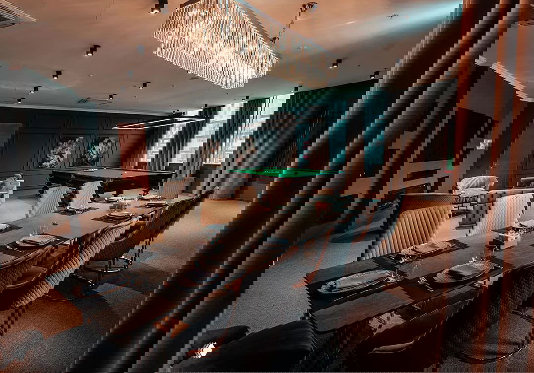 Элегантная ВИП‑комната с бильярдным столом и обеденной зоной: люстра, сервировка, мягкие кресла и большие окна создают уютную атмосферу.