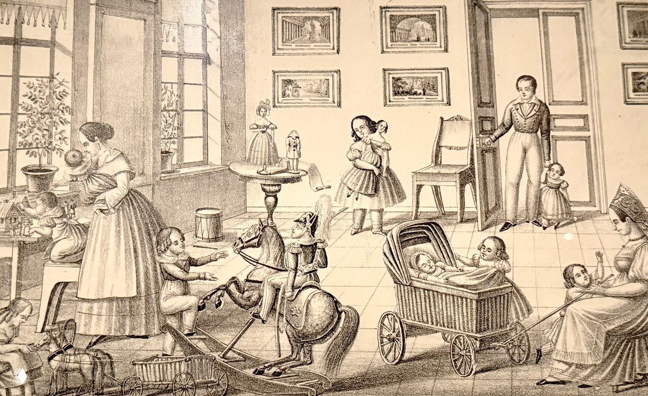 Чёрно‑белая гравюра с интерьером и детьми, играющими с игрушками и куклами — литография, иллюстрирующая бытовые сцены той эпохи в экспозиции.