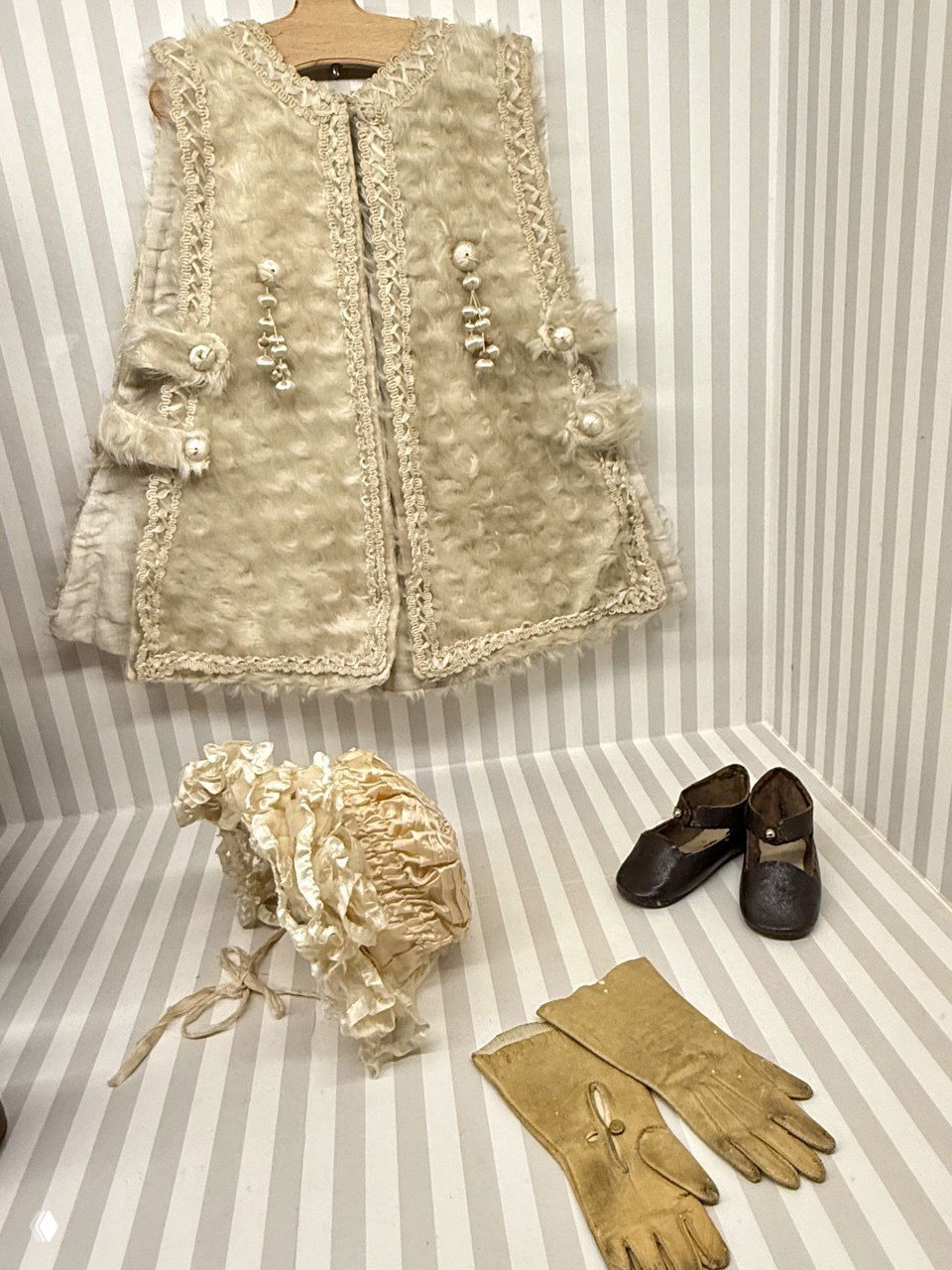 Детали кукольной одежды: жилет, шляпа, перчатки и туфельки на полосатой подложке — витрина с аксессуарами для кукол и их миниатюрной одеждой.