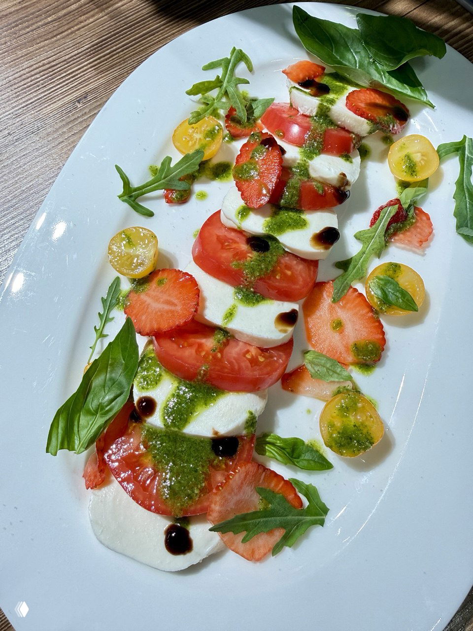 Тарелка капрезе: нарезанная моцарелла и томаты, листики базилика, соус песто и бальзамическая глазурь на белой овальной тарелке