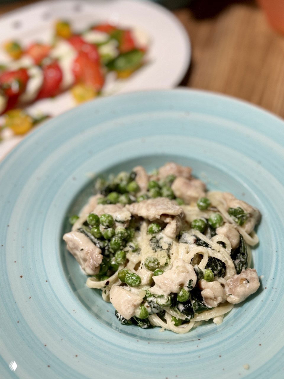 Порция пасты с зелёным горошком, кусочками курицы и сливочным соусом на голубой тарелке — готовое блюдо, сервированное в студии