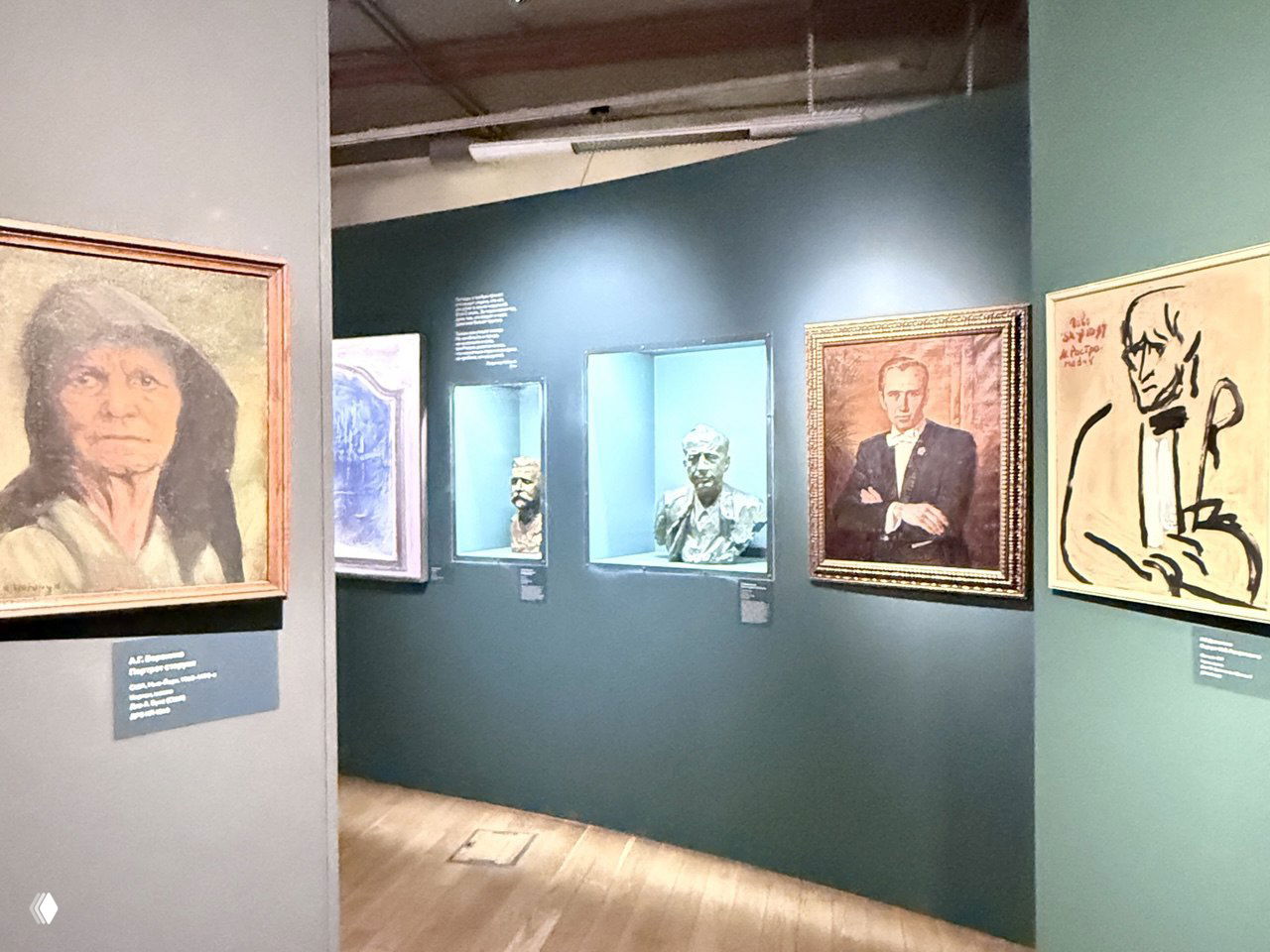 Просмотр экспозиции: картины и бюсты в нишах на зелёной стене, деревянный пол и свет экспозиции создают атмосферу небольшого музея.