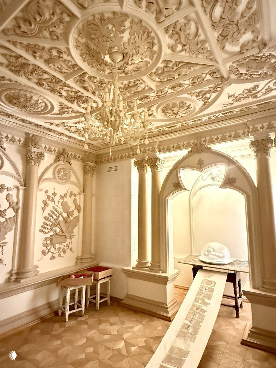 Парадный интерьер с декорированным лепным потолком и колоннами; на столе развёрнутый длинный свиток как часть инсталляции в восстановленном историческом интерьере.