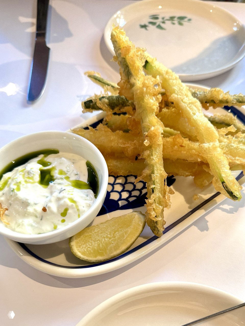 Цукини фри с соусом дзадзики и долькой лайма: хрустящие полоски цукини в темпуре, поданы на небольшом блюде с зелёным маслом и йогуртовым дипом.