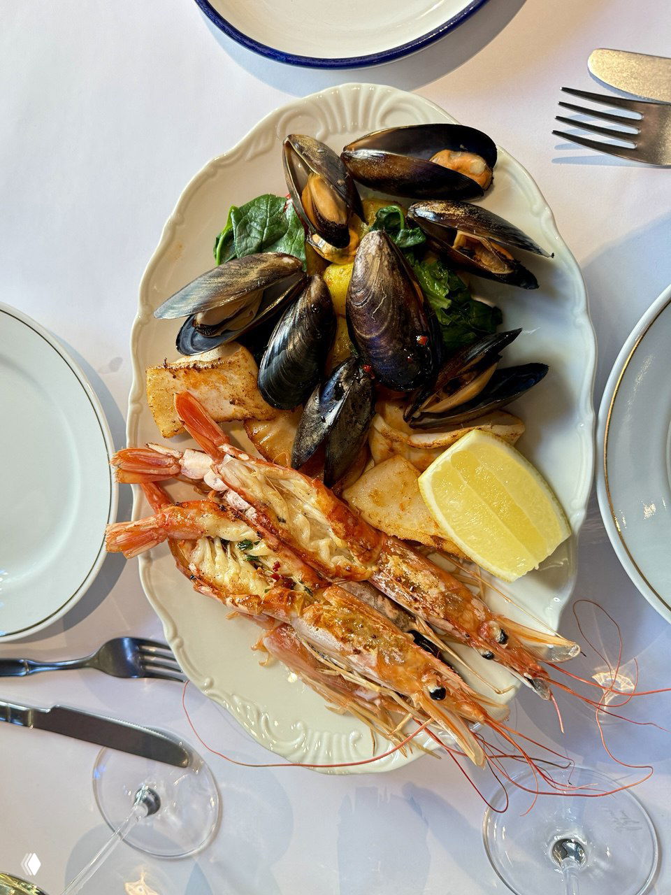 Плато с морепродуктами: жареные креветки, мидии и гарнир, поданы на белой тарелке с лимоном и зеленью, порция на двоих.