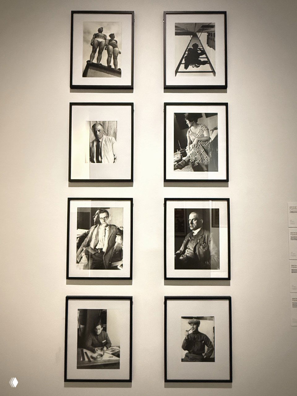 Ряд черно‑белых фотографий в рамках, смонтированных в сетку на стене выставочного зала, портреты и кадры из творческой биографии мастеров.