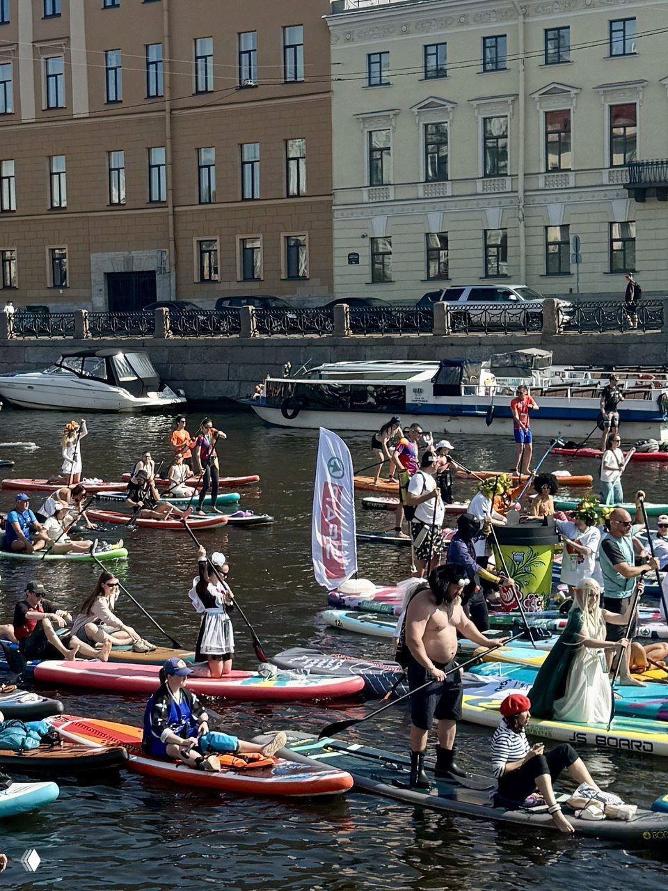 Множество людей на сапбордах в канале Петербурга — разноцветные доски, флаги и участники карнавала на воде летом.