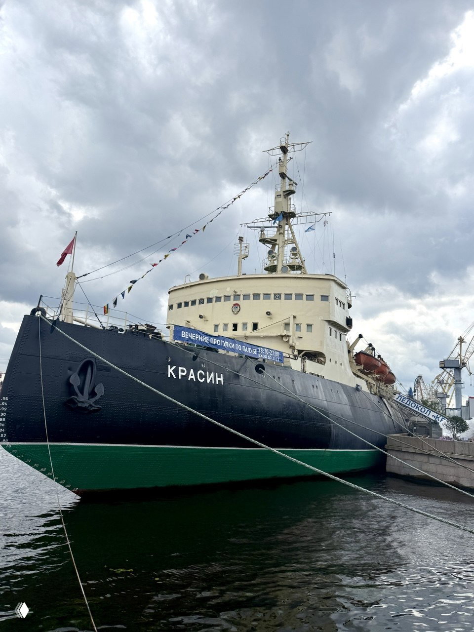 Ледокол «Красин» пришвартован у причала: крупный план носа судна с надписью «Красин», пасмурное небо над ним.