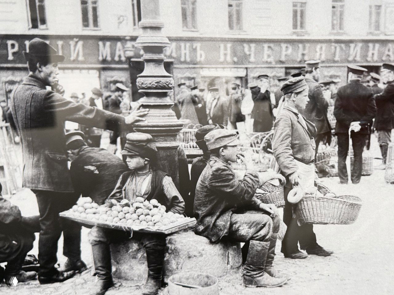 Документальная уличная фотография: дети‑продавцы с корзинами и лотками на площади, городская торговля и социальные условия конца XIX — начала XX века.