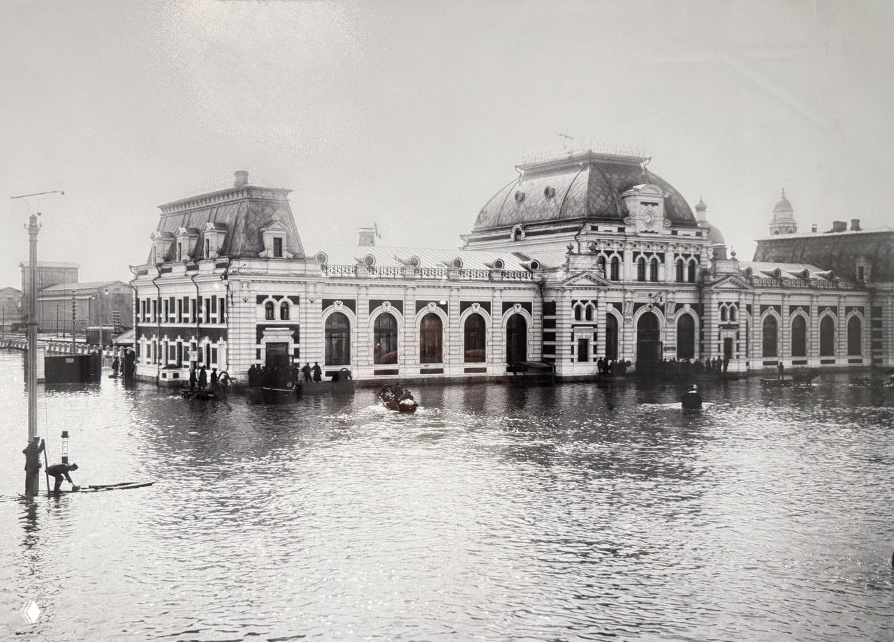 Панорамный архивный снимок наводнения 1908 года в Москве: затопленное здание и набережная, люди в лодках и вода, покрывшая городские улицы.