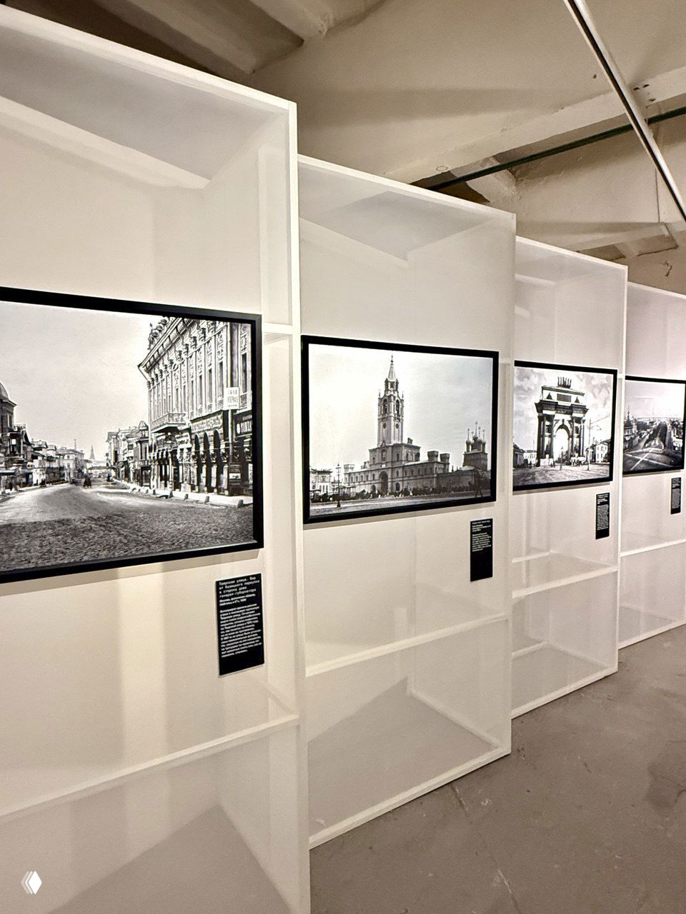 Интерьер экспозиции в Музее Москвы: белые стенды и рамы с историческими снимками городской архитектуры и улиц конца XIX — начала XX века.