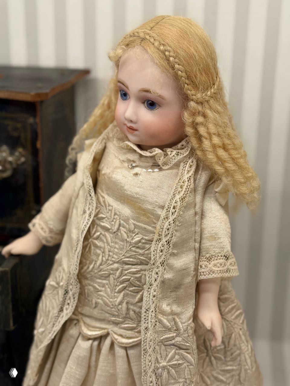 Крупный план фарфоровой куклы с тонкой росписью лица и сложной прической, платье с вышивкой и кружевами, музейная экспозиция.