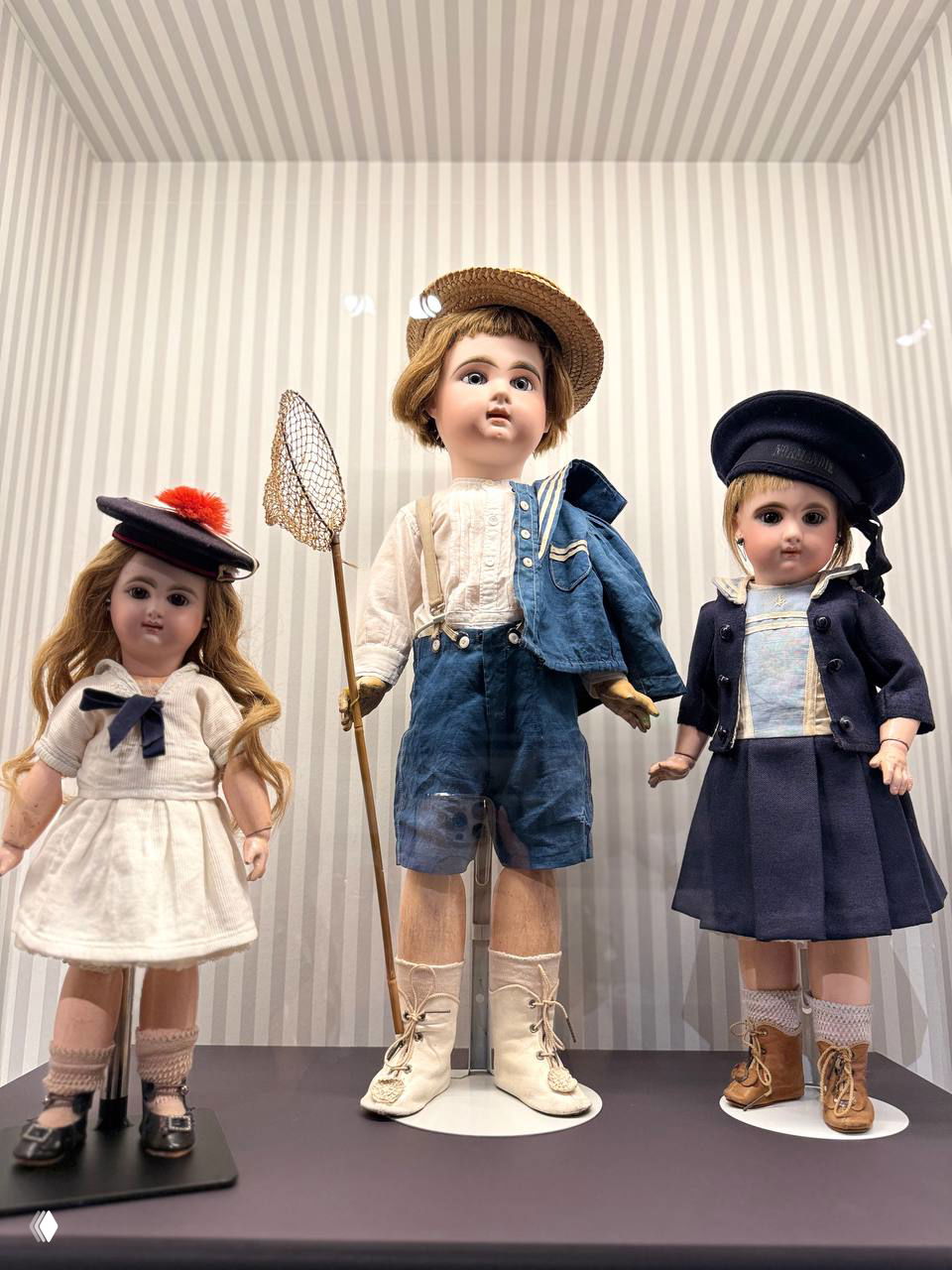 Группа кукол в витрине: мальчик в соломенной шляпе с сачком и две девочки в морском стиле — костюмы конца XIX–начала XX века.