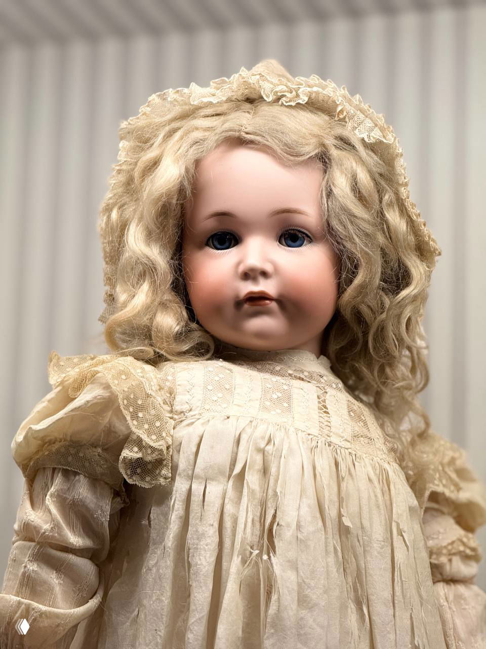 Портретный крупный план куклы с тонким фарфоровым лицом и светлыми локонами, подчёркнуты текстуры ткани платья и выражение лица.