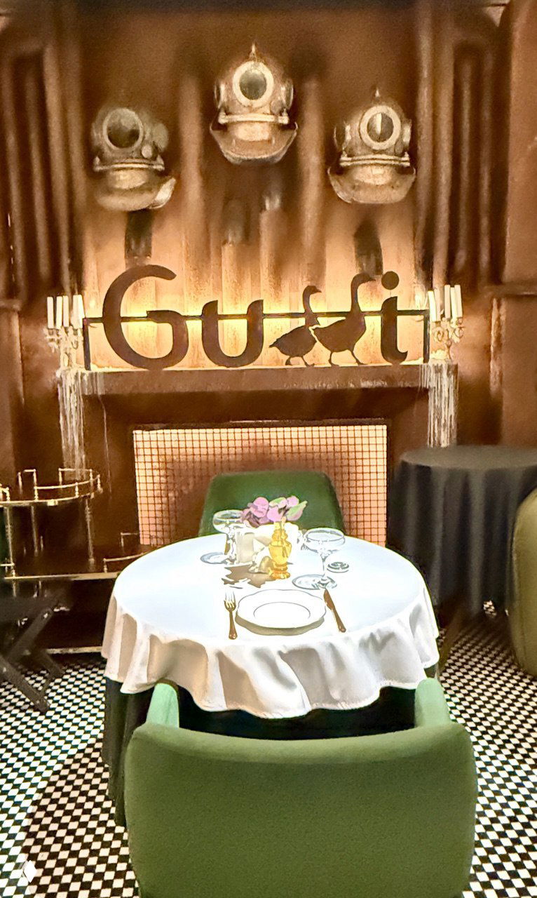 Сервировочный стол у настенной композиции с надписью Gussi: маленький столик с белой скатертью, аккуратная сервировка и фирменный декоративный фон с логотипом ресторана.