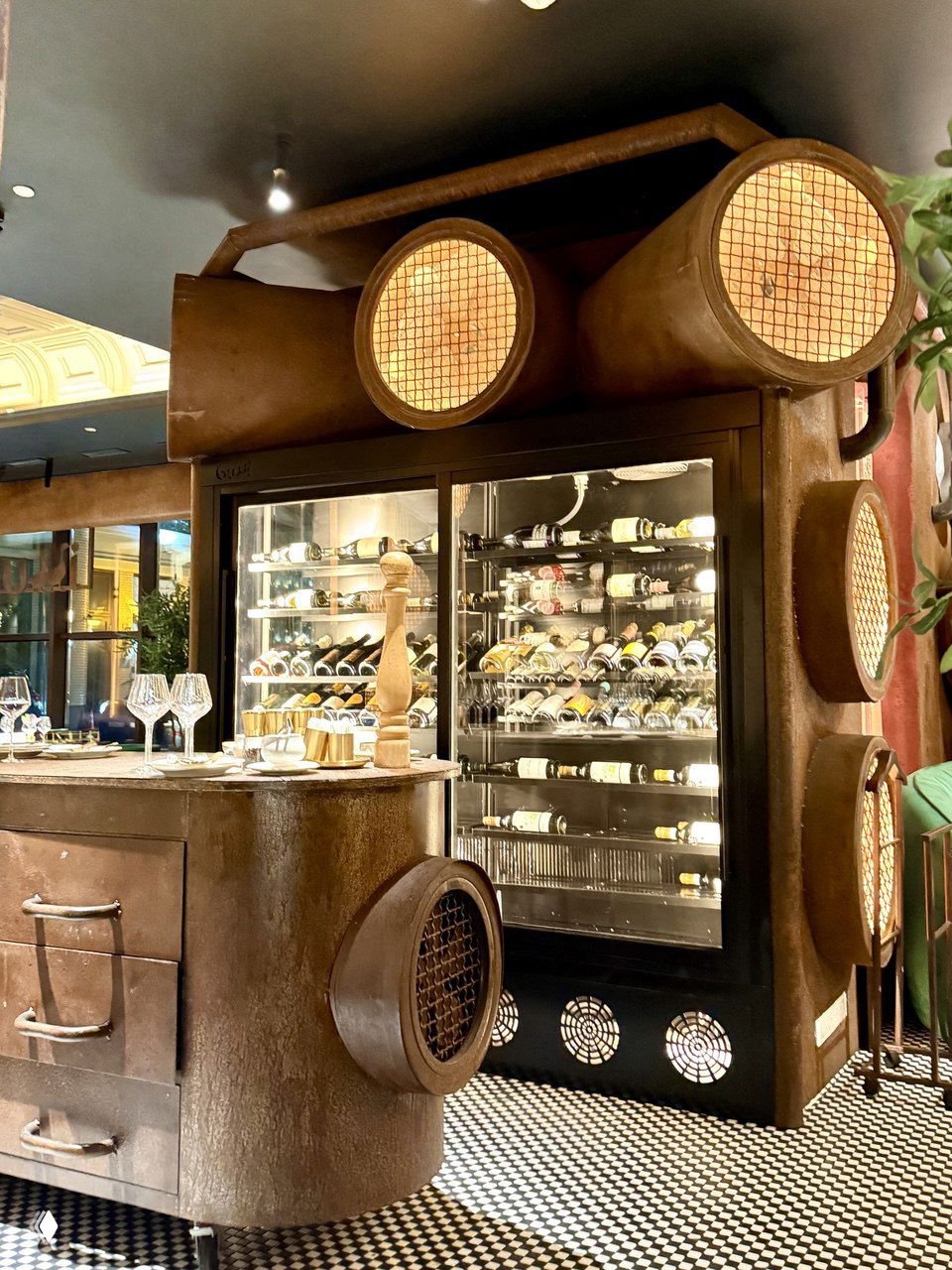 Винный холодильник и барная зона ресторана Gussi: стеклянная витрина с бутылками вина, металлические и стилизованные промышленные декоративные элементы вокруг стойки.