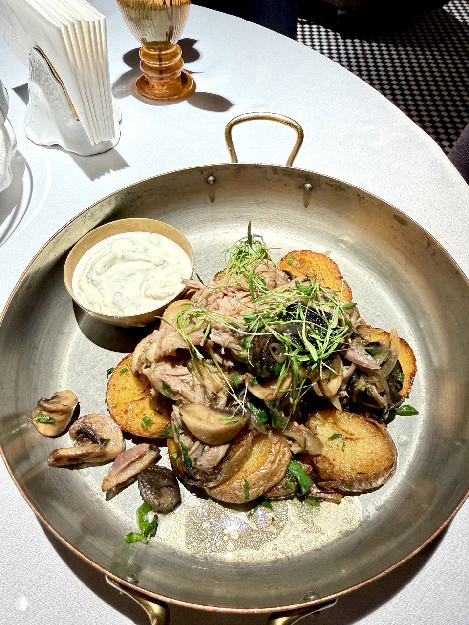 Тёплое основное блюдо: жареные картофельные кружочки, тёплая мясная часть с грибами, зелёная микрозелень и соус в большой металлической сковороде — плотная домашняя подача.