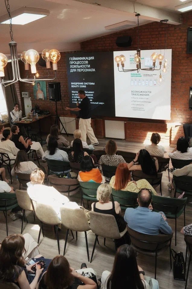 Ряд слушателей в зале: женщины и мужчины сидят в креслах, направив взгляд на сцену, выражения заинтересованности и концентрации.